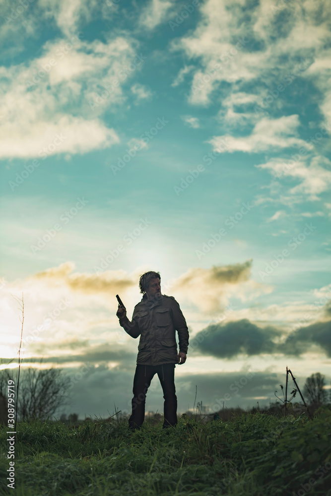 Man with handgun in countryside at sunset. Man with handgun in countryside at sunset.