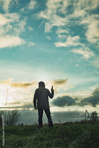 Man with handgun in countryside at sunset.