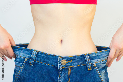 A slender woman shows her weight loss by wearing big jeans. liposuction.