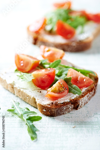 Tomato sandwich with cream cheese and fresh rocket on bright wooden background. Close up.