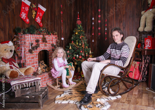 dad sits in a rocking chair and daughter sits on a rocking horse in New Year's decorations