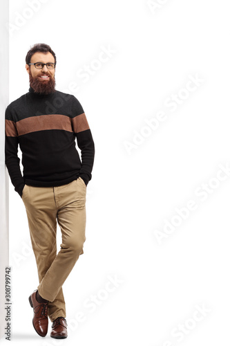 Bearded man in a turtleneck cardigan leaning on a wall