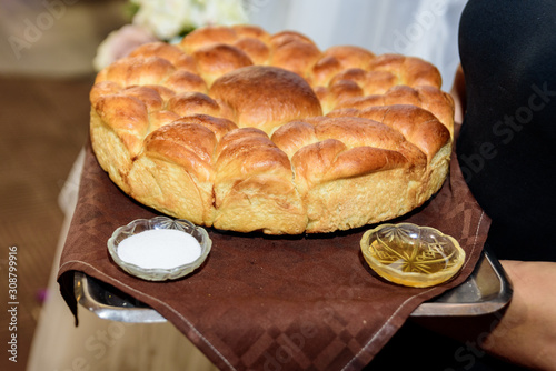 A woman holds a metal tray with fresh round bread and two plates of salt and honey. Bulgarian tradition, wedding.
