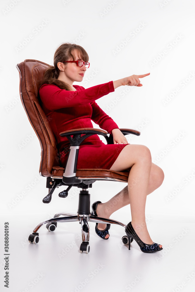 A girl in a red dress and red glasses sits in an office chair and gestures, pointing finger somewhere A girl in a red dress and red glasses sits in an office chair and gestures, pointing finger somewhere