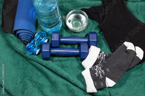 Home fitness items - a green towel, socks, a sports swimsuit, dumbbells, a hand massager, a rug, a bottle and a cup of water.