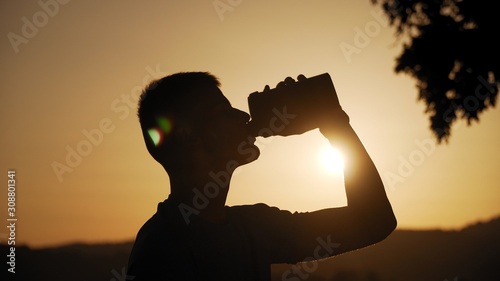 silhouette of fit young man drinking water with sun behind it in sunset