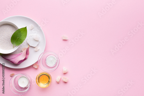 Spa composition with oils, sea salt, candles and tropical plants on a pastel pink background