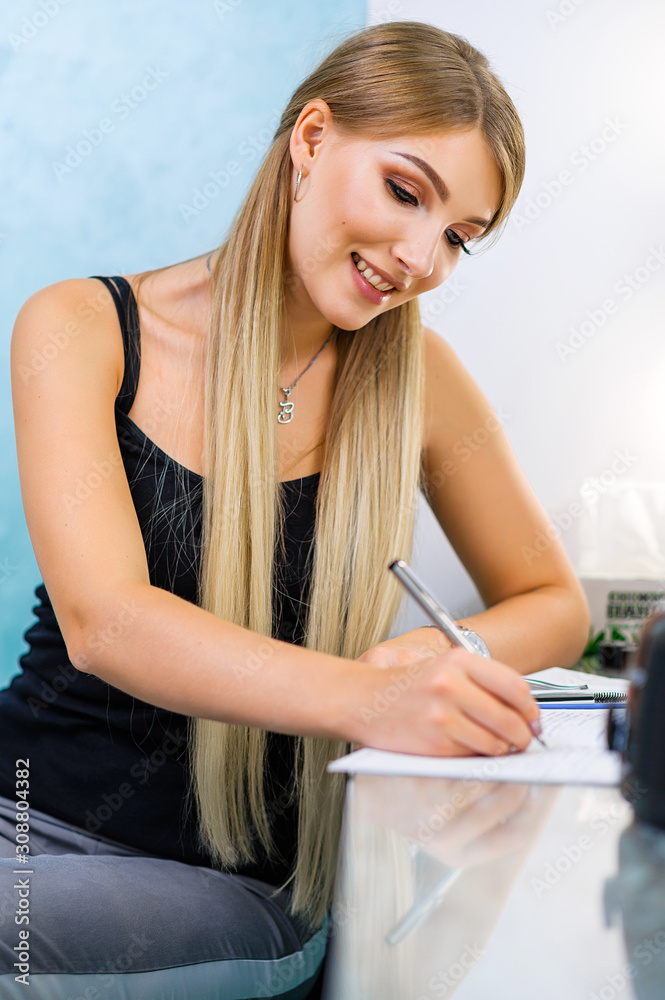 Beautiful attractive blonde in a working room. Girl at work. Girl takes notes in a notebook. Girl with a notebook Beautiful attractive blonde in a working room. Girl at work. Girl takes notes in a notebook. Girl with a notebook