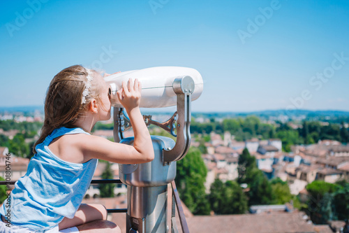 Beautiful girl looking at coin operated binocular on terrace at small town in Tuscany