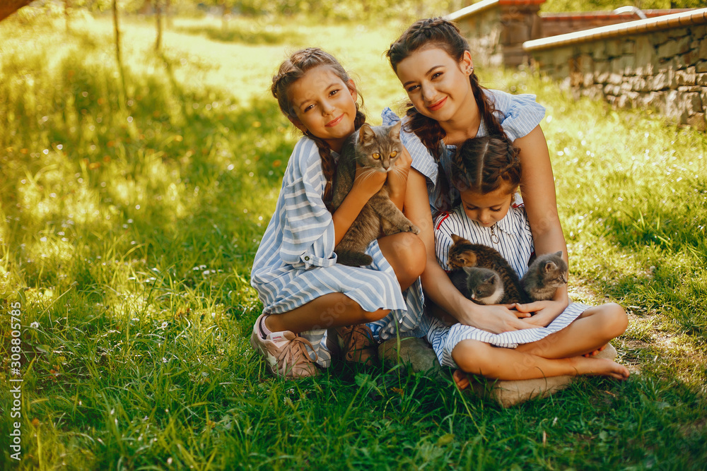 three beautiful and cute girls in blue dresses with beautiful hairstyles and make-up sitting in a sunny green garden and playing with a cats three beautiful and cute girls in blue dresses with beautiful hairstyles and make-up sitting in a sunny green garden and playing with a cats