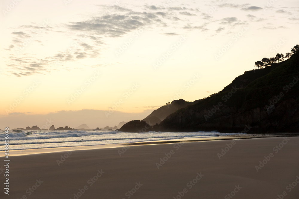 Hermoso amanecer en playa de Aguilar con cielo anaranjado con nubes en Muros de Nalón, costa de Asturias, España