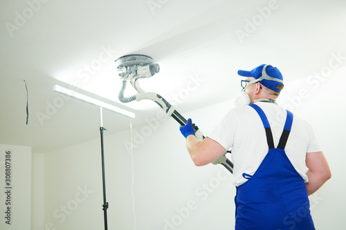 Painter work with ceiling. polishing and sanding the surface after putty for painting photo