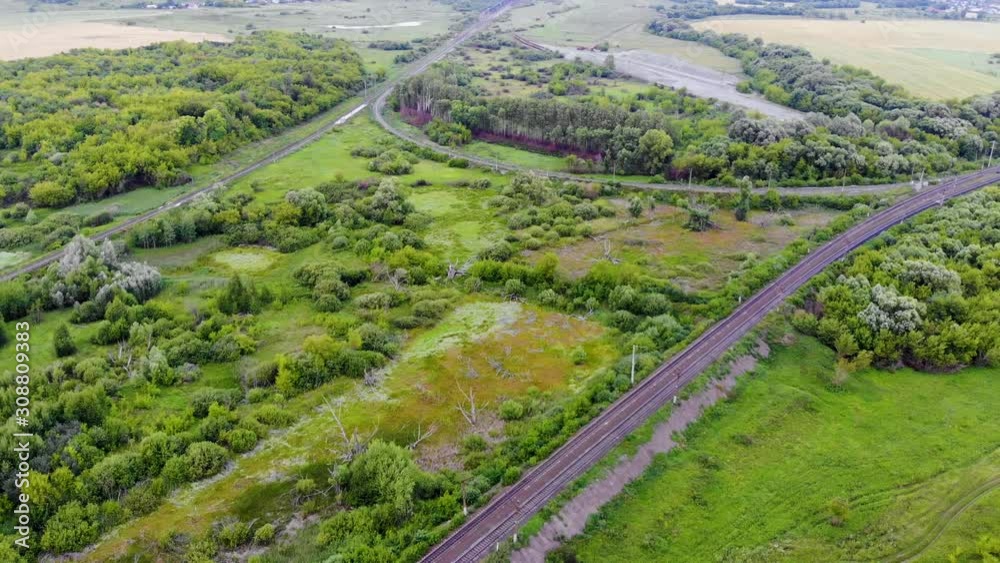 Aerial shot of a railway junction connected by a rounded railway path. A freight train is approaching in the distance. Ways connect distant objects of the country. Taken by drone Aerial shot of a railway junction connected by a rounded railway path. A freight train is approaching in the distance. Ways connect distant objects of the country. Taken by drone