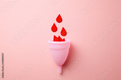 Silicone menstrual cup. Women's health and alternative hygiene. Cup with drops of blood on a pink background. photo