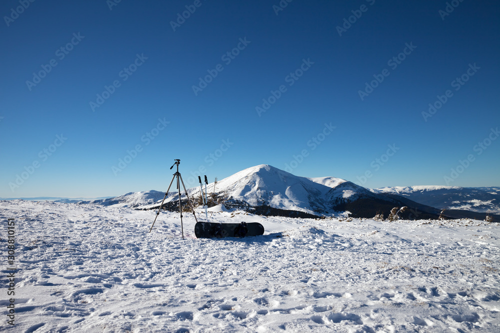 Obraz premium Tripod for photography camera, ski poles, snowboard on snow and snow-capped mountains