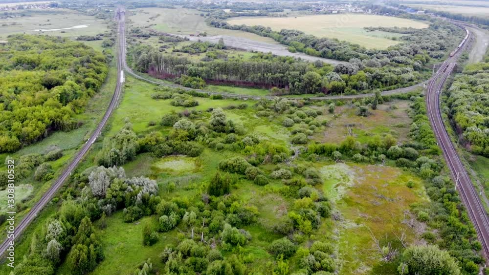 Aerial shot of a railway junction connected by a rounded railway path. A freight train is approaching in the distance. Ways connect distant objects of the country. Taken by drone