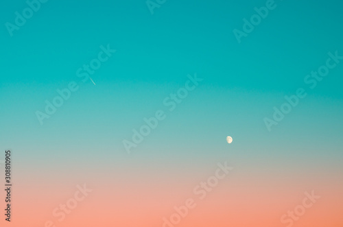 The Moon and a plane in the clear duotone gradient blue evening sky