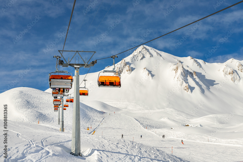 Ski lift ropeway on hilghland alpine mountain winter resort on bright sunny day. Ski chairlift cable way with people enjoy skiing and snowboarding.Banner panoramic wide view of downhill slopes Ski lift ropeway on hilghland alpine mountain winter resort on bright sunny day. Ski chairlift cable way with people enjoy skiing and snowboarding.Banner panoramic wide view of downhill slopes