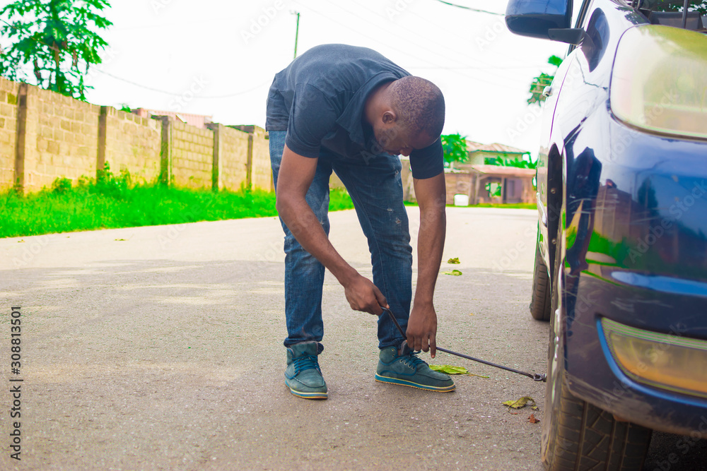 Young African man wearing a hard hat sitting while trying to change his tyre Young African man wearing a hard hat sitting while trying to change his tyre