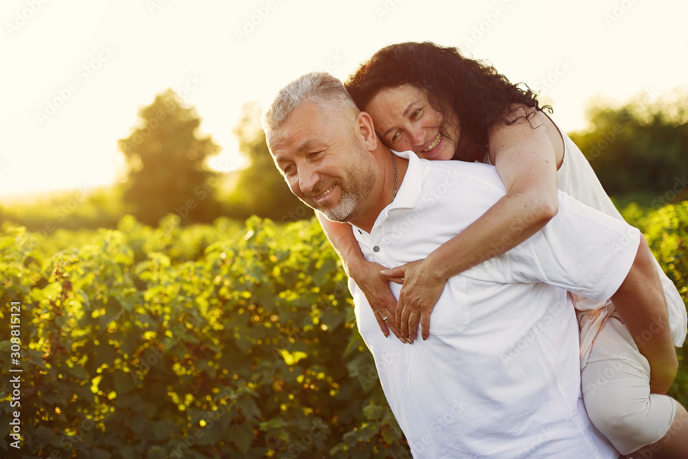 Aduld couple in a summer field. Handsome senior in a white shirt. Woman in a white dress Aduld couple in a summer field. Handsome senior in a white shirt. Woman in a white dress