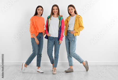 Group of young women in stylish jeans near white wall
