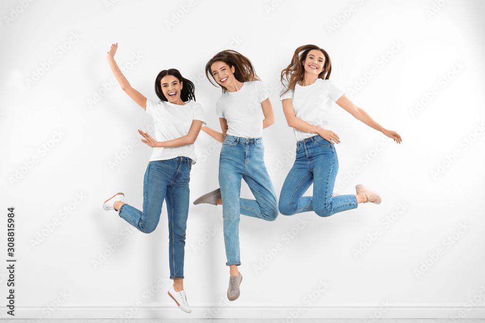 Group of young women in stylish jeans jumping near white wall Group of young women in stylish jeans jumping near white wall