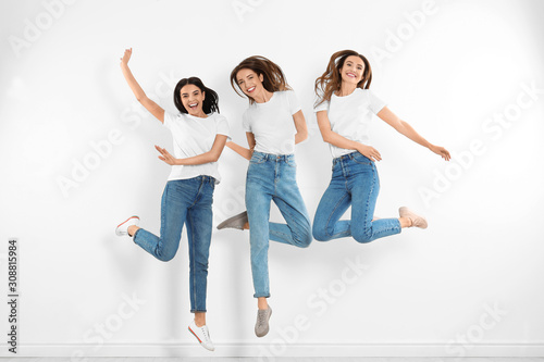 Group of young women in stylish jeans jumping near white wall