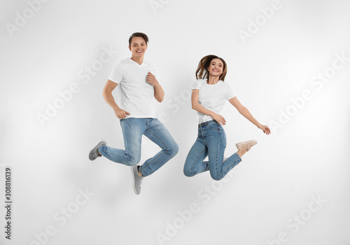 Young couple in stylish jeans jumping near white wall