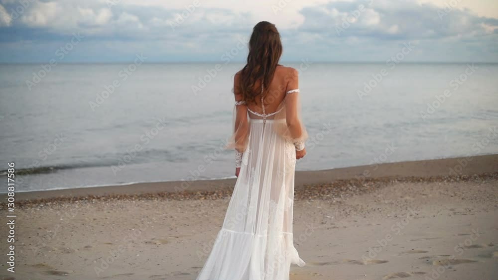 Back of a beautiful bride in a wedding dress walking on the seashore Back of a beautiful bride in a wedding dress walking on the seashore