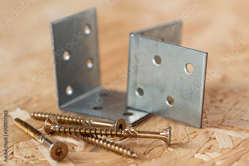 Two galvanized angle brackets and self drilling screws lying on chip board. Blurred background. photo