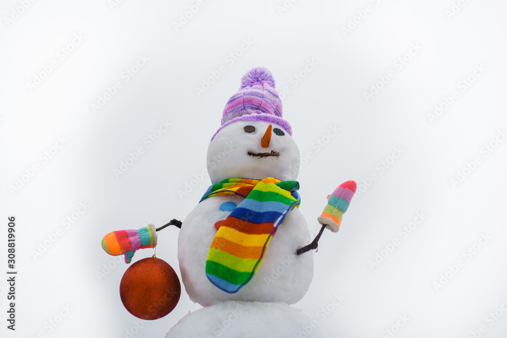 Smiling snowwoman with Christmas toy. Merry Christmas and Happy new year. Snowman hold new year ball. Snow man in winter hat. Christmas background with snowman. Funny snowman in stylish hat and scarf.