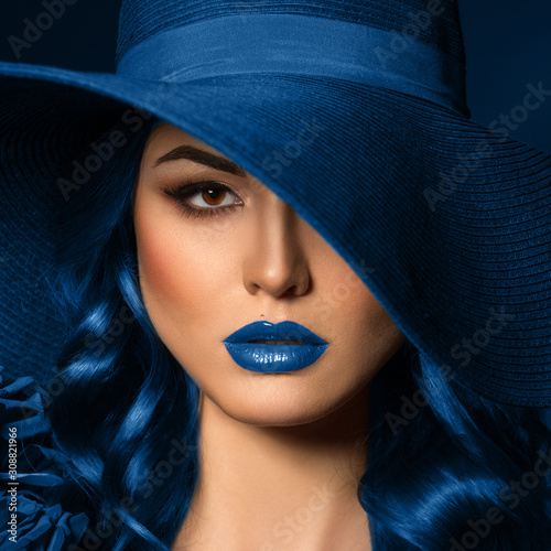Portrait of a beautiful woman with blue lips in a hat, toned in color of the year 2020, classic blue.
