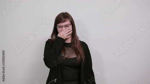 Portrait of confused young woman looking aside and covering nose with hand isolated on grey wall background in studio. People sincere emotions, lifestyle concept. photo