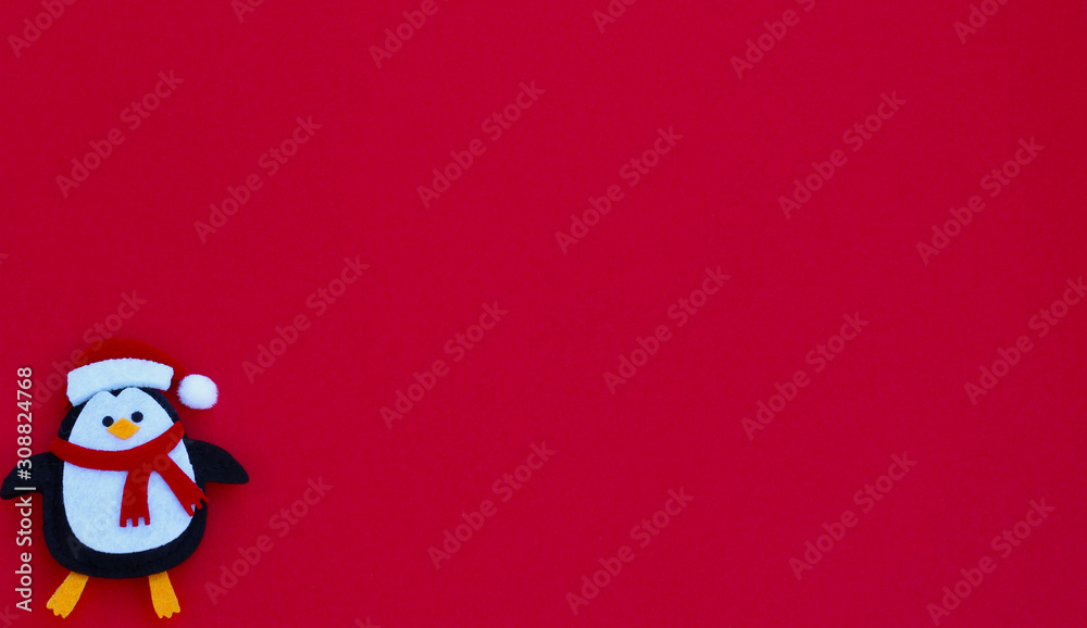 felt crafted penguin with Santa Claus hat laying flat on a festive red background