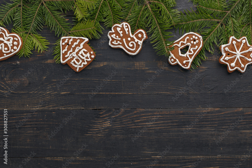 Christmas composition of homemade gingerbread and spruce branches on a black wooden background.