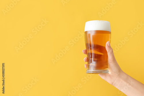 Hand with glass of beer on color background