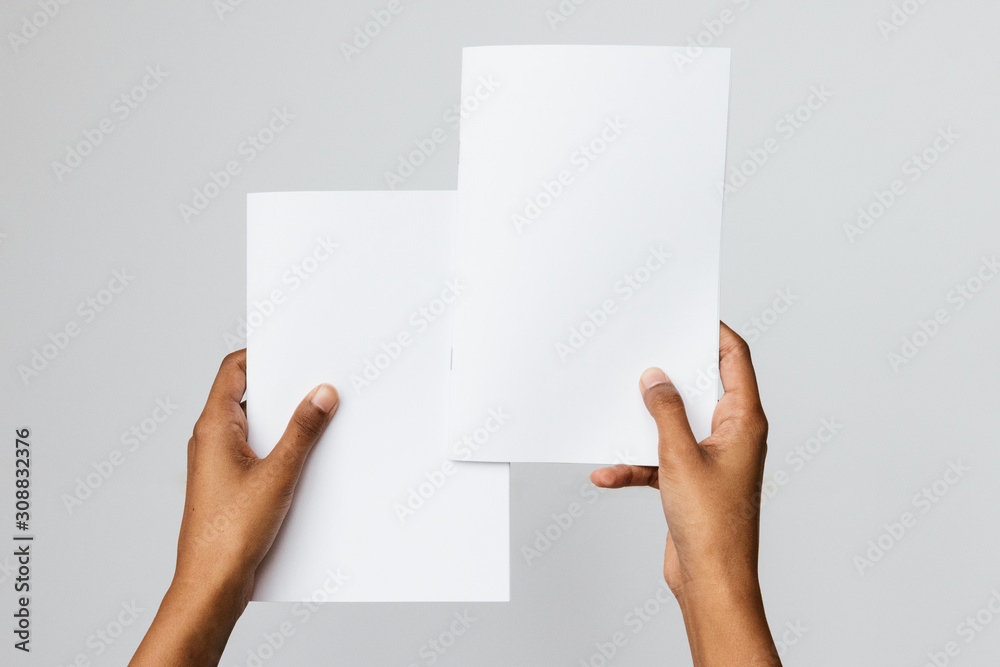 Black, Southeast Asian or ethnic model holding two blank mock-ups or dummies of A4 or letter sized brochures or reports. Studio shot on white. Ideal to place art of two publications for comparison. Black, Southeast Asian or ethnic model holding two blank mock-ups or dummies of A4 or letter sized brochures or reports. Studio shot on white. Ideal to place art of two publications for comparison.