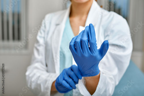 Close up of a female doctor putting a blue latex gloves on a clinic background. photo