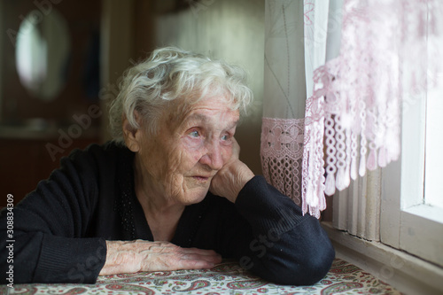 Old russian woman sits in a house near the window.
