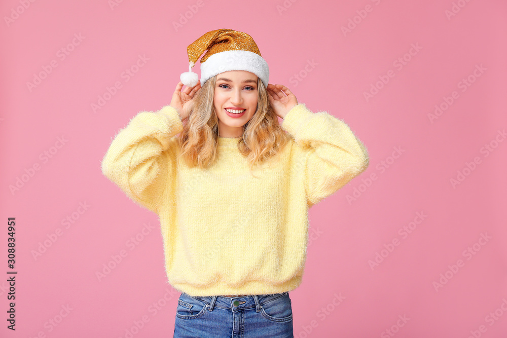 Happy young woman in winter clothes and Santa Claus hat on color background Happy young woman in winter clothes and Santa Claus hat on color background