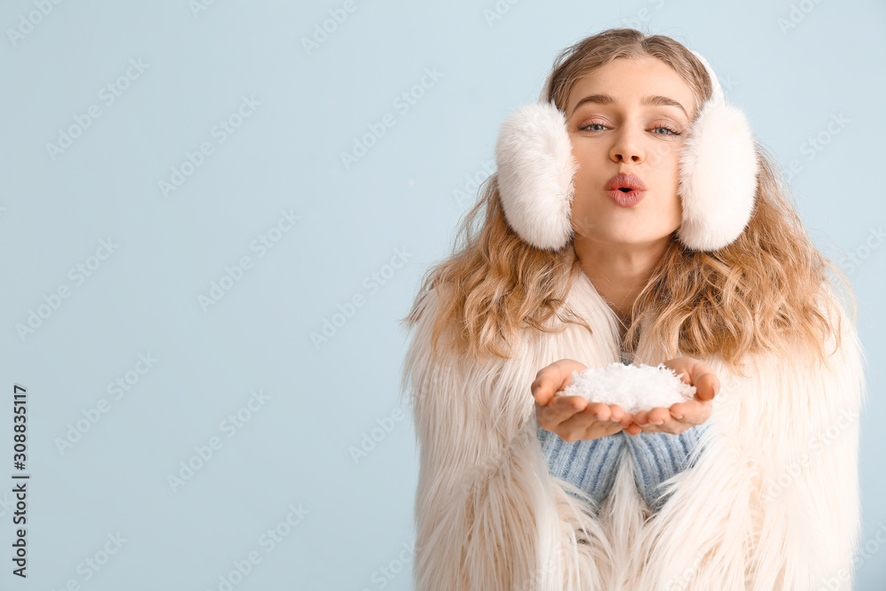 Happy young woman in winter clothes blowing snow on color background Happy young woman in winter clothes blowing snow on color background