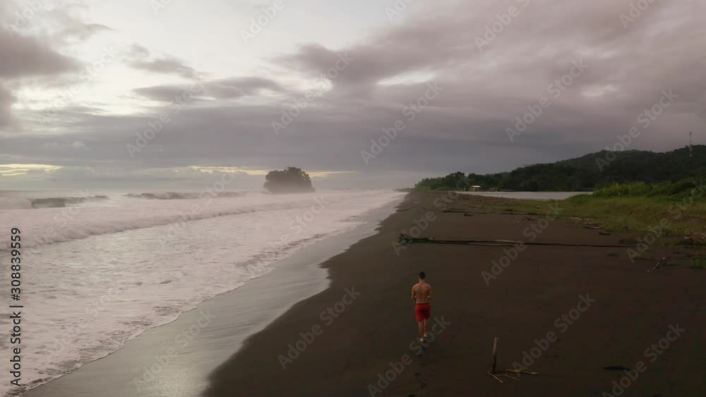 Young white man walks early evening on a blacksand beach in Colombia. Young white man walks early evening on a blacksand beach in Colombia.