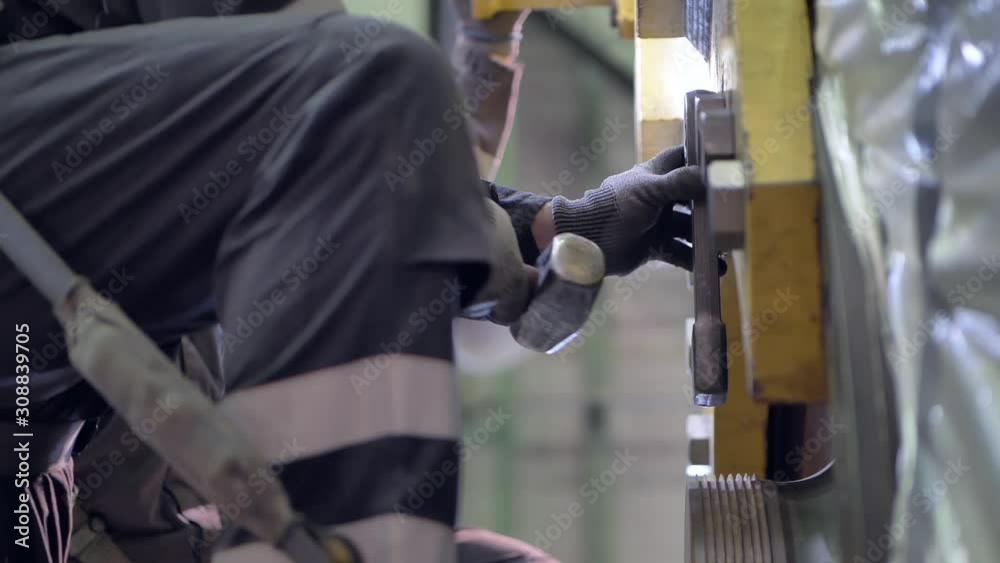 Male worker releasing tight heavy bolts from industrial metalwork, hitting nut to break seal loose. Male worker releasing tight heavy bolts from industrial metalwork, hitting nut to break seal loose.