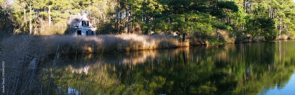 Run down small house surrounded by trees, tall grass, and small body of water. Run down small house surrounded by trees, tall grass, and small body of water.