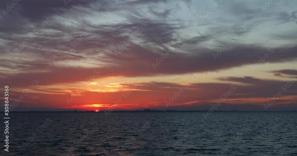 A colorful sunrise paints a cloudy sky with color over San Carlos Bay with Fort Myers Beach, Florida on the horizon in this seamless motion background video time lapse