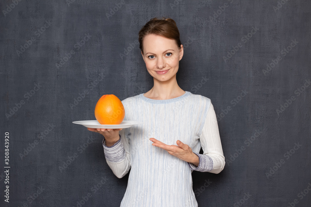 Portrait of happy young woman pointing at plate with grapefruit Portrait of happy young woman pointing at plate with grapefruit
