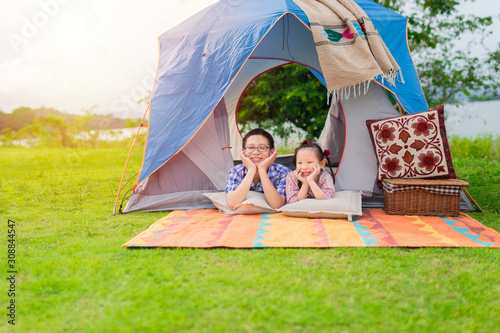 couple asian children stay on floor and rest chin on hand in tent, they make face  show crazy emotion, they camping and picnic on nature background, they feeling happy and funny in relax time photo