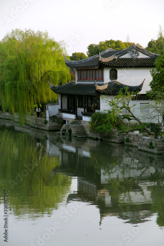 Classical houses in Jiangnan, China. The white walls and black tiles are matched with green weeping willows. The reflection of the river reflects the poetic and picturesque scenery.