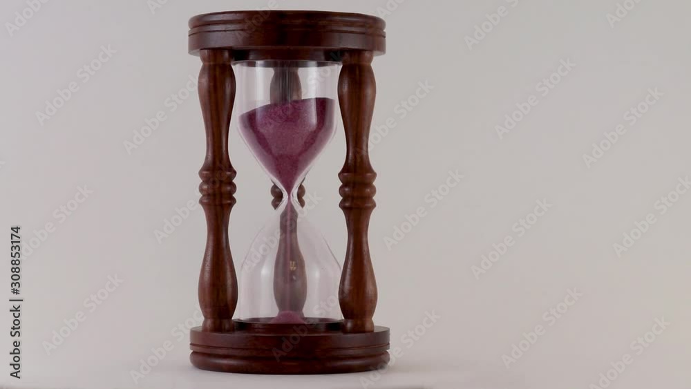 Sand inside an hour glass slowly falling counting down the seconds and minutes symbology of time is running out beautiful wood frame with red and purple sand flowing  
