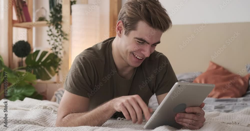 Young man laughing while using digital tablet in bed at home Young man laughing while using digital tablet in bed at home